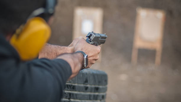 Detail back view of shooter holding gun in hand and shooting on target, close up. Shooting range