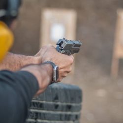 Detail back view of shooter holding gun in hand and shooting on target, close up. Shooting range